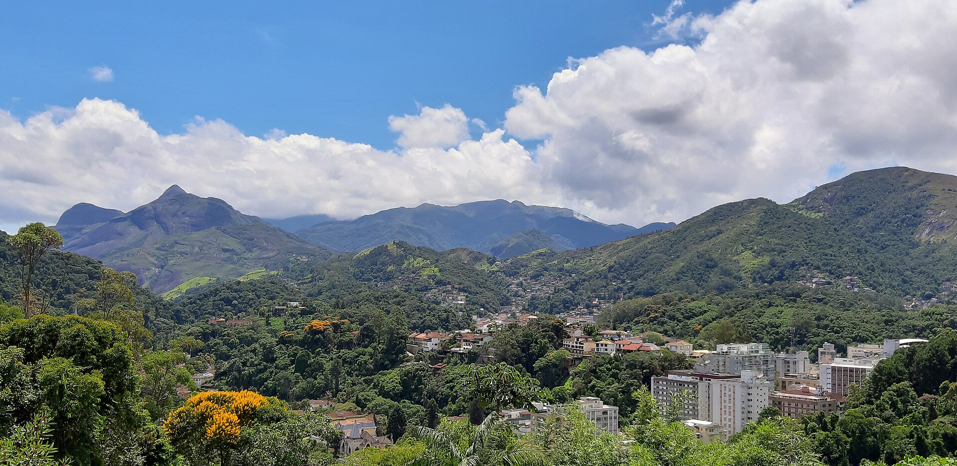 Vista panorâmica de bairros e montanhas de Petrópolis em um dia de céu azul.