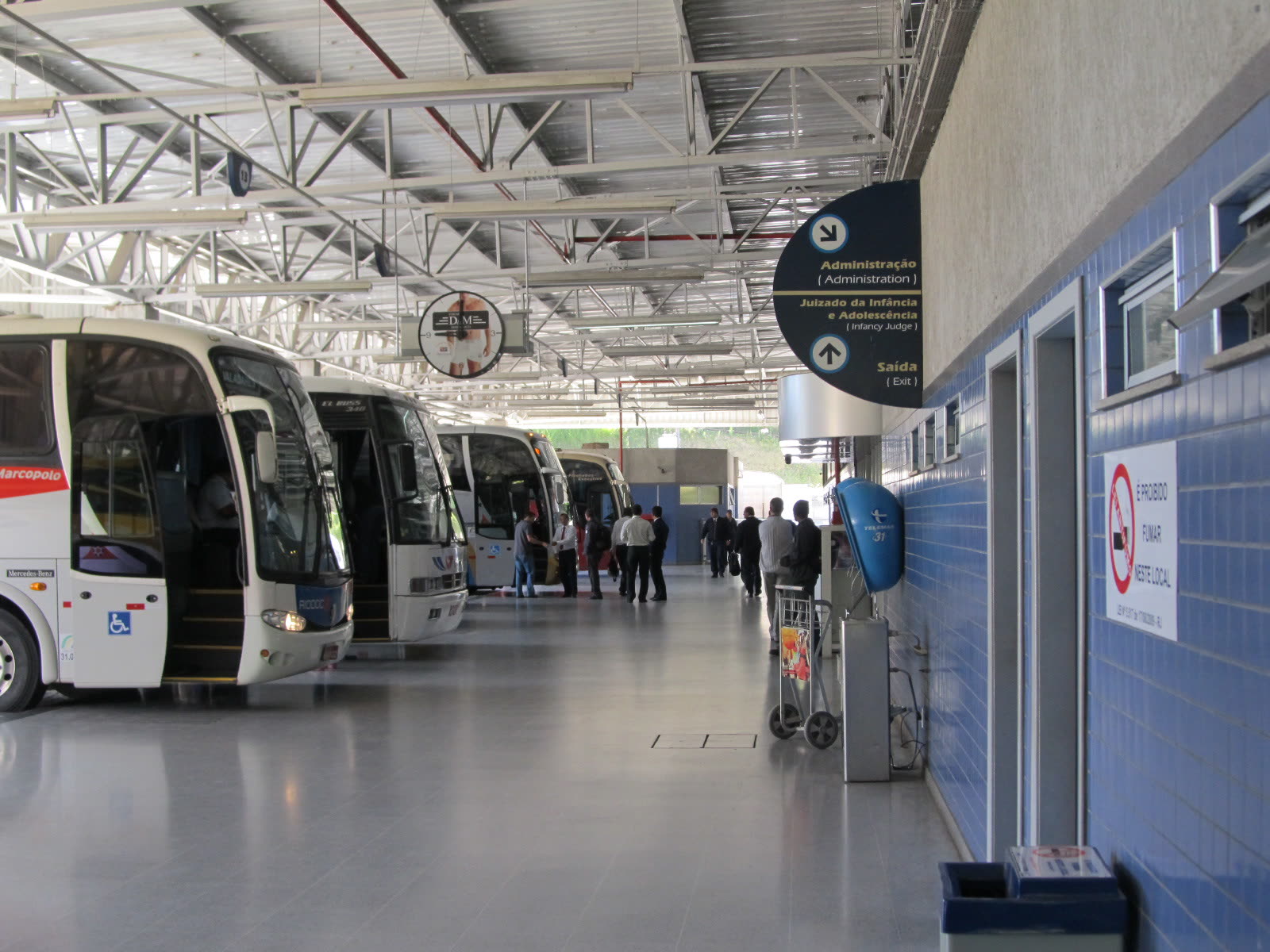 Ônibus, passageiros e placas de direção no interior da Rodoviária de Petrópolis.